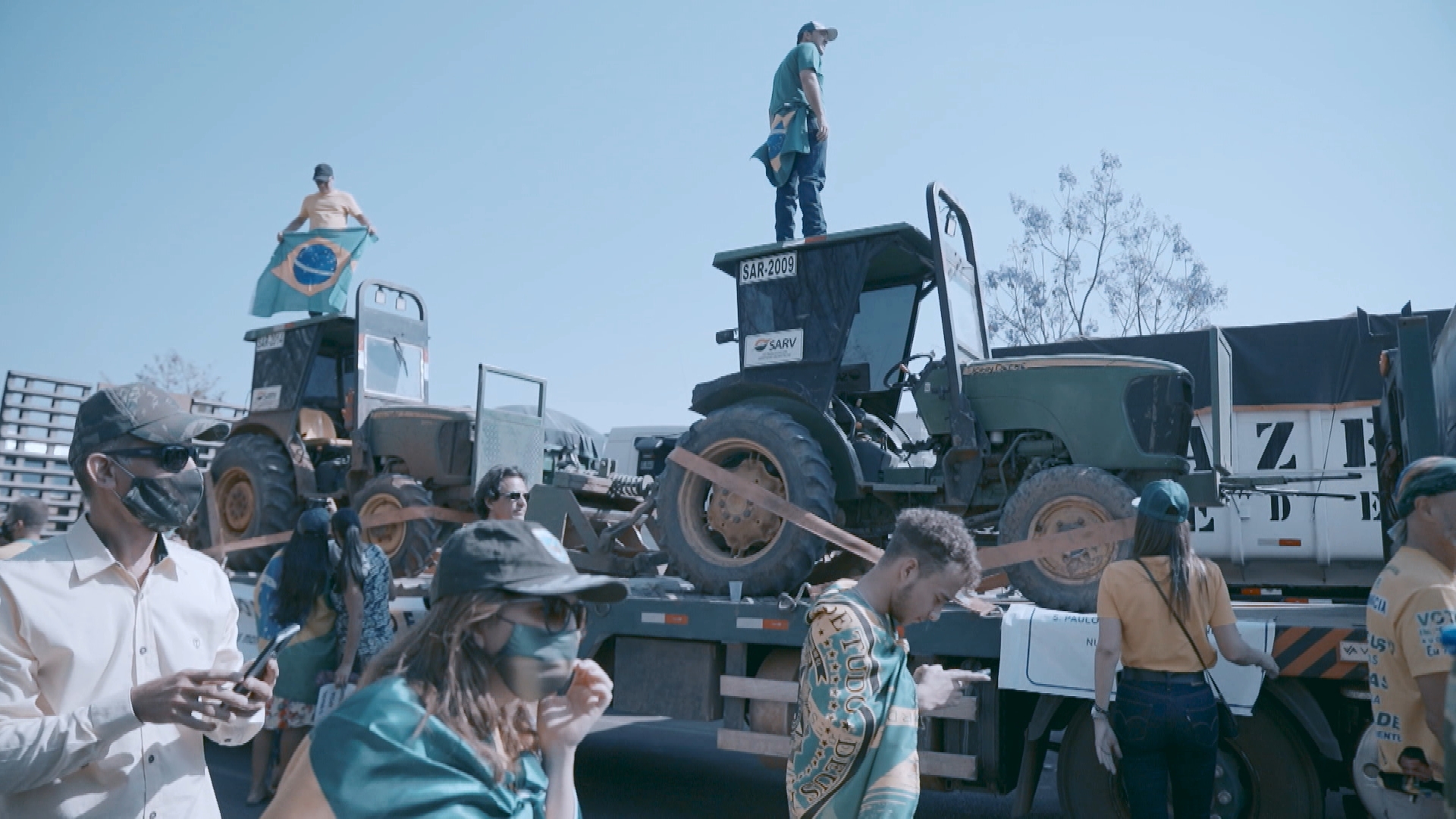 lidé s brazilskými vlajkami pochodují podél vozu vezoucím traktory